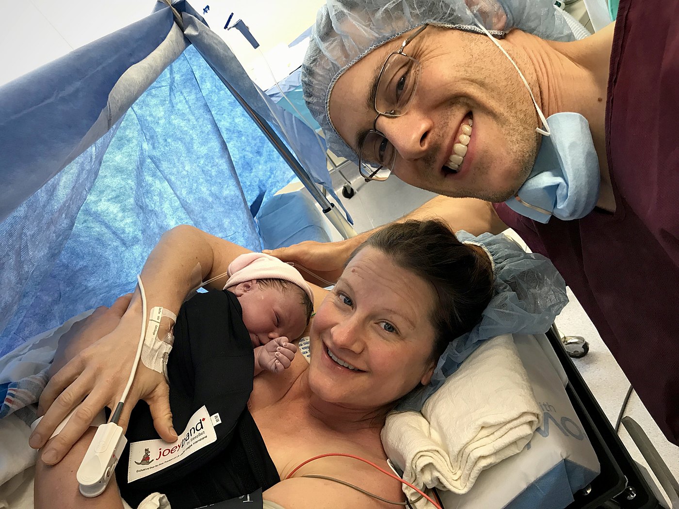 Newborn secured skin-to-skin on a parent in the operating room with a Joeyband